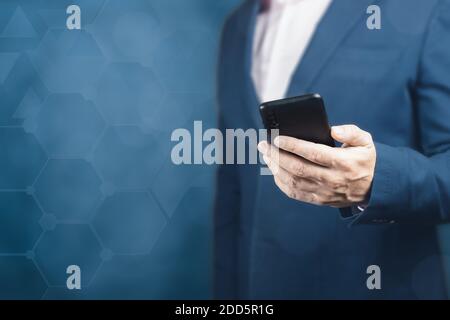 l'uomo in una tuta sta tenendo cellulare. Business online. Uomo d'affari che tiene il telefono. Uomo che usa lo smartphone su sfondo blu scuro sfocato Foto Stock