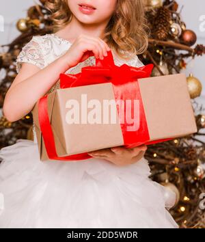 Una ragazza in un abito chic si erge con un regalo di Capodanno nelle sue mani sullo sfondo di un albero di Capodanno Foto Stock