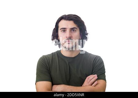 Ritratto di bruna serio giovane uomo, capelli lunghi ricci, mantiene le braccia piegate aspetto sicuro e messo a fuoco sulla fotocamera, isolato su sfondo bianco Foto Stock