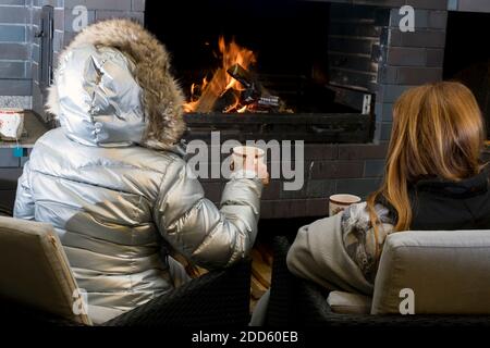 due donne in abiti invernali che bevono tè di fronte camino esterno Foto Stock