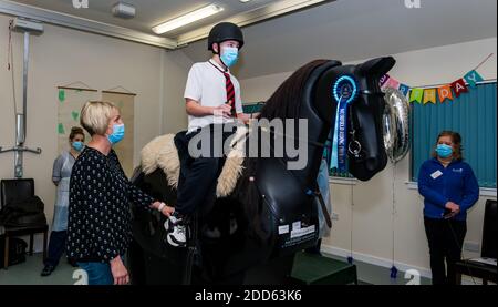 East Lothian, Scozia, Regno Unito, NHS Lothian & Muirfield Riding Therapy celebrano 10 anni di ippoterapia: Il fisioterapista Heather Falconer ha aperto la strada al Children’s Therapeutic Riding Service, che offre un'equitazione terapeutica gratuita a bambini e adulti con disabilità. Il servizio è stato il primo in Scozia. Oreo, un cavallo meccanico, permette ai giovani di ricevere una divertente fisioterapia. Charlie Kay, di 13 anni che ha partecipato sin dall'inizio, si trova a cavallo del simulatore meccanico Racewood Foto Stock