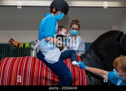 East Lothian, Scozia, UK, NHS Lothian & Muirfield Riding Therapy festeggia 10 anni di ippoterapia: Il fisioterapista Heather Falconer ha aperto la strada al Children’s Therapeutic Riding Service, che fornisce gratuitamente un'equitazione terapeutica a bambini, giovani e adulti con disabilità. Il servizio è stato il primo in Scozia per i bambini con problemi di mobilità, equilibrio, tono muscolare e coordinazione. Oreo, un cavallo meccanico, permette ai giovani di divertirsi con la fisioterapia. Jamie Burns, di 2 anni, cavalca il simulatore meccanico di cavalli Racewood con Lizzie, fisioterapista Foto Stock