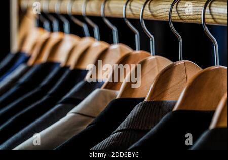 Abiti da uomo in diversi colori appesi su appendiabiti in un negozio di abbigliamento al dettaglio, primo piano. Camicie uomo, tuta appesa su scaffale Foto Stock