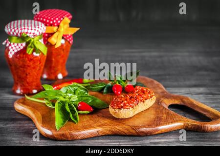 Tradizionale pepe balcanico spalmato - ajvar, servito su un rustico tagliere di legno (fuoco selettivo) Foto Stock