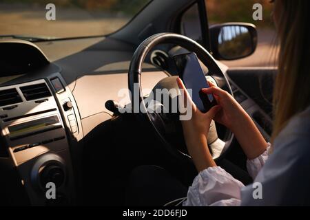 Vista ravvicinata della giovane donna che sta testando sul telefono cellulare durante la guida e senza concentrarsi sulla strada Foto Stock