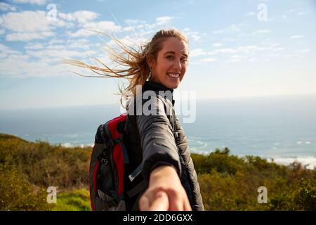 Punto di vista ripresa di attiva giovane donna trekking in campagna via mare incoraggiando off screen partner a seguirla tenendo la mano Foto Stock