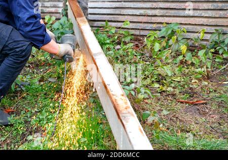 L'operatore taglia la struttura metallica con una smerigliatrice angolare a disco, creando un pennacchio luminoso di molte scintille calde. Foto Stock