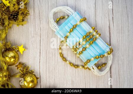 Composizione con maschera medica blu corona virus e decorazione invernale con palline d'oro su sfondo di legno offuscato. Buon Natale in covid-19 pa Foto Stock