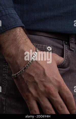 mano di una persona nella tasca dei suoi pantaloni, utilizza un bracciale d'argento sul polso, dettagli delle texture Foto Stock