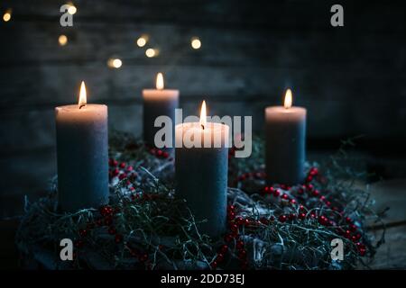 Quattro candele che bruciano su una corona di avvento con decorazione di Natale rossa, tradizione di portare luce nella stagione invernale, sfondo nero rustico di legno w Foto Stock