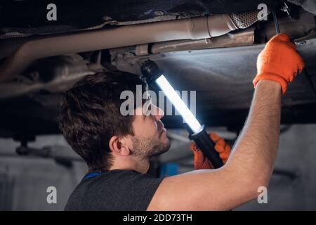 Uomo in uniforme usando una torcia controlla la parte inferiore di la macchina Foto Stock