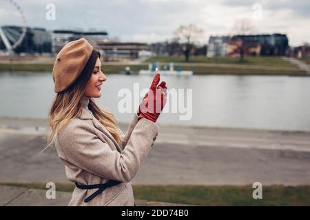 Donna elegante che prende selfie al telefono camminando lungo il molo vicino al fiume Wisla a Cracovia, Polonia godendo del paesaggio. Foto Stock