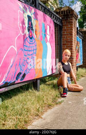 Un forte artista tatuato si trova sulla strada di fronte il suo murale dipinto Foto Stock