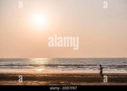 Persona jogging sulla spiaggia Miramar al tramonto, Panjim, Goa, India Foto Stock