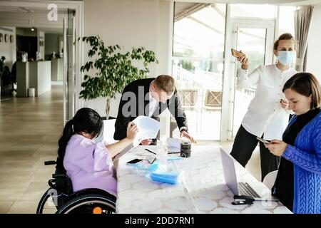 Colleghi che lavorano in ufficio con uno seduto in sedia a rotelle Foto Stock