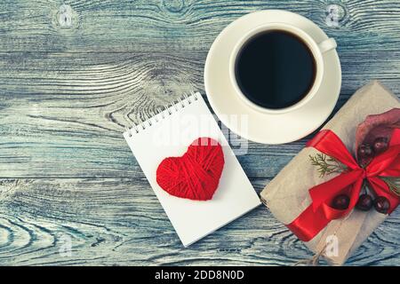 Confezione regalo, blocco note con un cuore e una tazza di caffè su sfondo grigio-blu in legno. Foto Stock