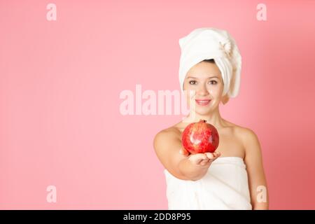 mock up, un melograno maturo sul palmo di una giovane donna in sfocatura su uno sfondo rosa Foto Stock