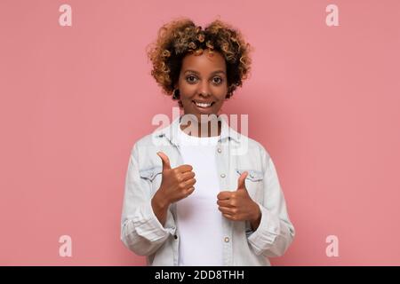 Giovane bella donna afroamericana con capelli ricci indossando abiti casual facendo felici pollici su gesto con la mano. Approvare il concetto di scelta Foto Stock