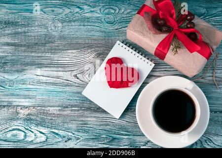 Sfondo romantico e accogliente con cuore rosso, confezione regalo e tazza di caffè. Foto Stock