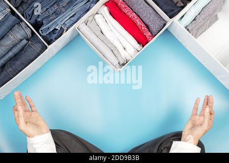 Le mani della donna che si siedono in posa del loto, meditando, mentre puliscono la casa, smistando e riordinando i vestiti. Vista dall'alto Foto Stock