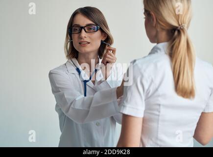 Il medico ascolta il battito cardiaco del paziente attraverso uno stetoscopio su uno sfondo chiaro vista ritagliata Foto Stock