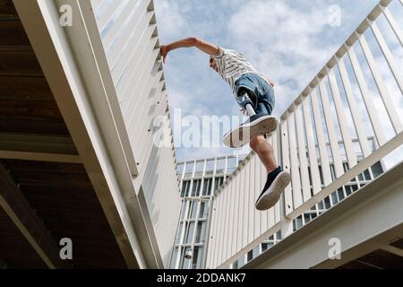 Vista ad angolo basso dell'uomo con arto artificiale che salta in mezzo ponte ringhiera in città Foto Stock