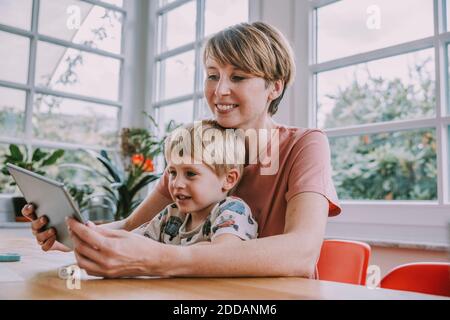 Madre che usa il tablet digitale con il figlio mentre si siede a casa Foto Stock