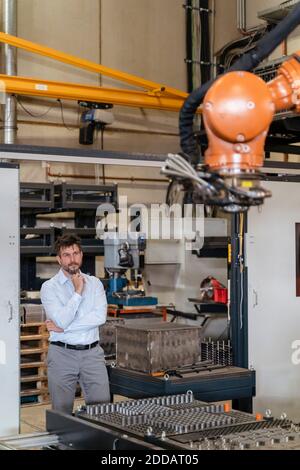 Uomo d'affari che monitora la macchina con braccio robotizzato mentre si trova in fabbrica Foto Stock