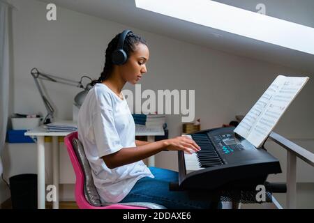 Ragazza adolescente che suona il pianoforte mentre si siede a casa Foto Stock