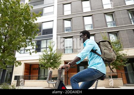 Uomo sorridente che ascolta musica mentre si è in viaggio in bicicletta in città Foto Stock