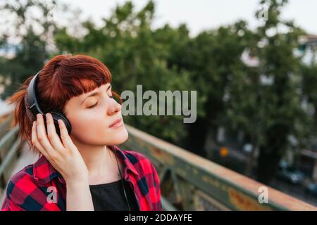 Donna rossa con occhi chiusi che ascolta la musica attraverso le cuffie Foto Stock