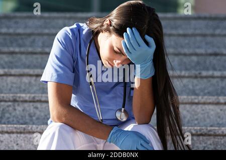 Young Doctor indossando guanti protettivi seduti con la testa in mano su scala Foto Stock