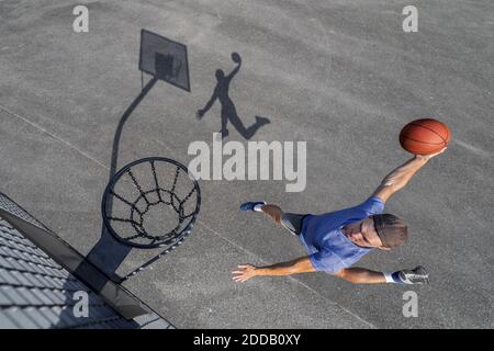 Giovane uomo che dunking palla in cerchio mentre gioca a basket giorno di sole Foto Stock