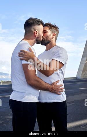 Affettuosa coppia gay baciando sul ponte contro il cielo Foto Stock