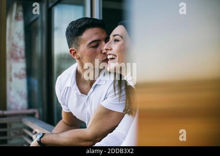 Ragazzo baciando la donna mentre si appoggia alla ringhiera del balcone Foto Stock