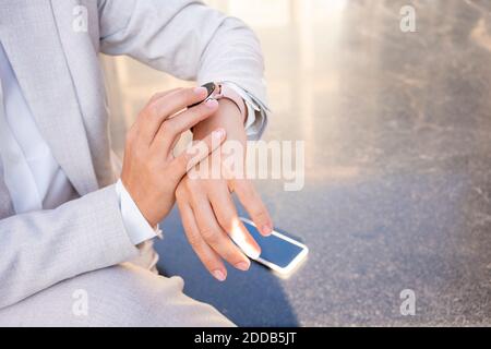 Donna che controlla il tempo sull'orologio da polso mentre si siede sulla panca a. città Foto Stock