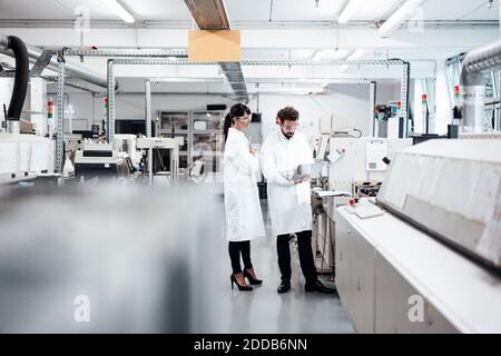 Gli scienziati maschili e femminili discutono sopra il laptop da macchina a. laboratorio Foto Stock