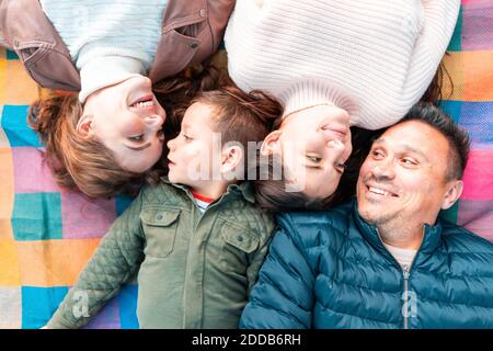 Direttamente sopra la vista di una famiglia sorridente che si guarda l'un l'altro mentre sdraiato su coperta da picnic nel parco Foto Stock