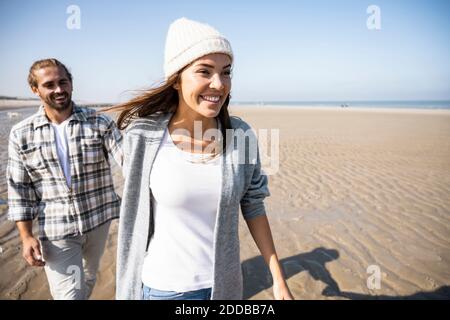 Giovane donna che tiene la mano dell'uomo mentre cammina sulla spiaggia Foto Stock