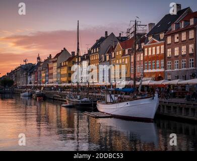 Danimarca, Copenhagen, Barche ormeggiate lungo la passeggiata di Nyhavn al tramonto con fila di case storiche in background Foto Stock