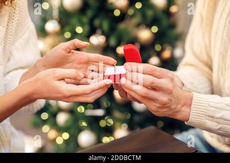 Vista ritagliata di uomo che tiene scatola di gioielli con anello di nozze e facendo proporre alla sua donna. Coinvolgimento delle persone contro lo sfondo sfocato dello spazio di copia Foto Stock