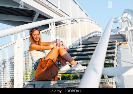 Donna sorridente seduto su una scala al parco Foto Stock