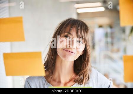 Marrone capelli donna matura guardando le note adesive bastone on materiale in vetro Foto Stock