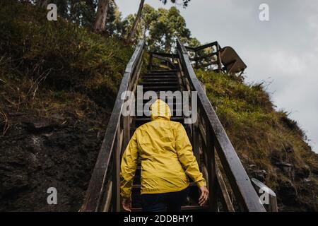 Vista posteriore della donna in scala di arrampicata impermeabile durante la pioggia stagione Foto Stock