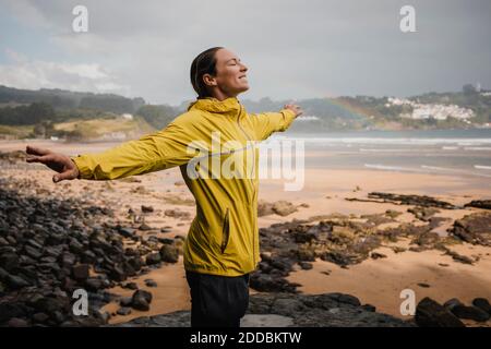 Donna sorridente in impermeabile giallo in spiaggia durante la stagione delle piogge Foto Stock