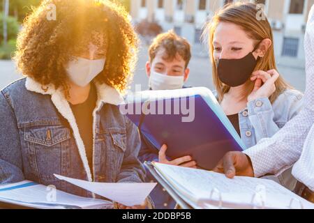 Studenti di sesso maschile e femminile che indossano una maschera protettiva mentre discutono le note nel campus universitario Foto Stock