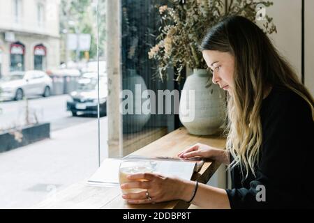 Donna d'affari che legge la rivista mentre beve il caffè alla caffetteria Foto Stock