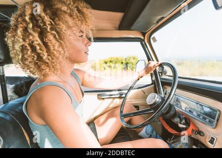 Giovane bionda donna afro seduta in un vecchio veicolo fuoristrada Foto Stock