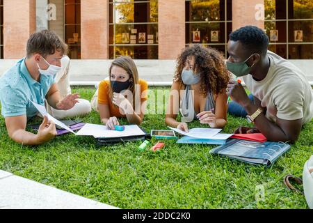 Studenti di sesso maschile e femminile che indossano una maschera di sicurezza durante la discussione erba nel campus universitario Foto Stock