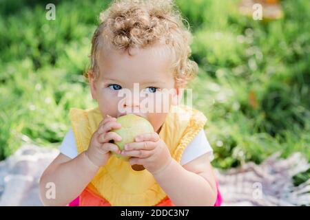 Carino ragazza del bambino che mangia frutta mentre sedendo sull'erba a. parcheggio Foto Stock